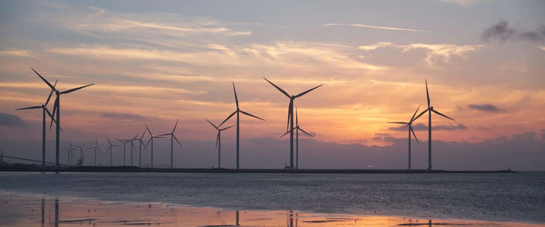 Wind Turbines On The Shoreline Silhouette Against A Vibrant Sunset, Promoting Renewable Energy. Wind Turbines On The Shoreline Silhouette Against A Vibrant Sunset, Promoting Renewable Energy.